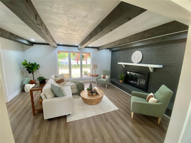 living area featuring baseboards, beam ceiling, a brick fireplace, and wood finished floors