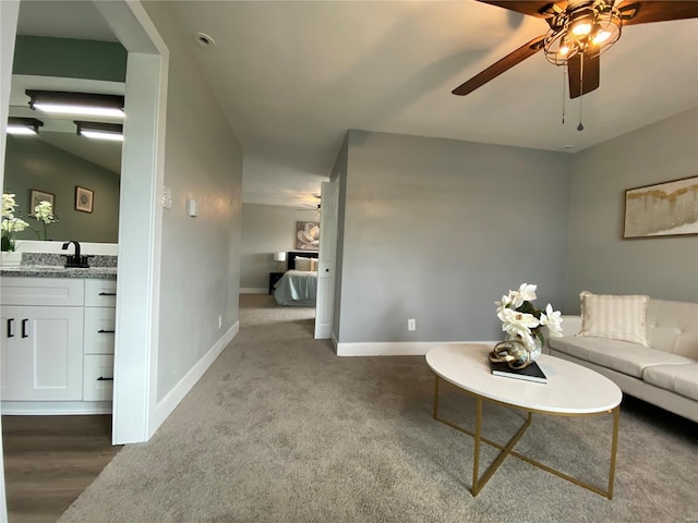 carpeted living area with baseboards, a ceiling fan, and a sink
