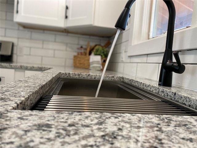 room details featuring backsplash, light stone countertops, a sink, and white cabinets