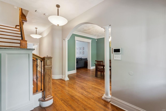 hallway with wood finished floors, arched walkways, decorative columns, baseboards, and crown molding