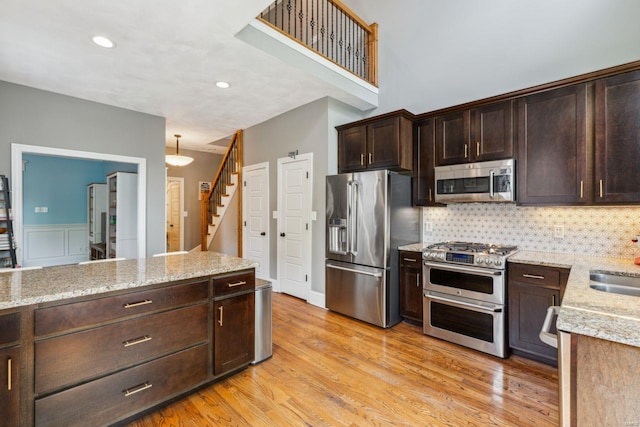 kitchen with stainless steel appliances, dark brown cabinetry, light wood-type flooring, light stone countertops, and backsplash
