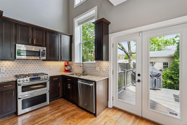 kitchen with light stone countertops, a sink, decorative backsplash, a wealth of natural light, and appliances with stainless steel finishes