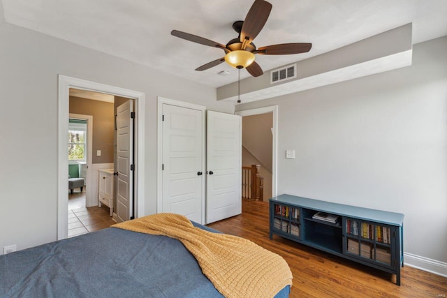 bedroom with a closet, a ceiling fan, visible vents, wood finished floors, and ensuite bathroom