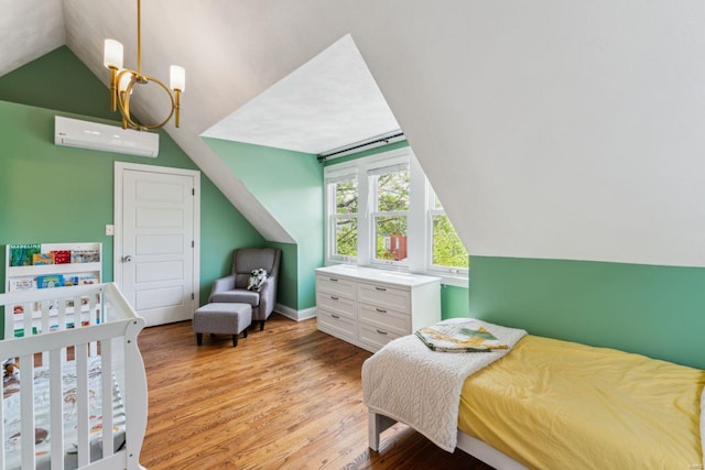 bedroom with light wood-type flooring, a wall unit AC, vaulted ceiling, and baseboards