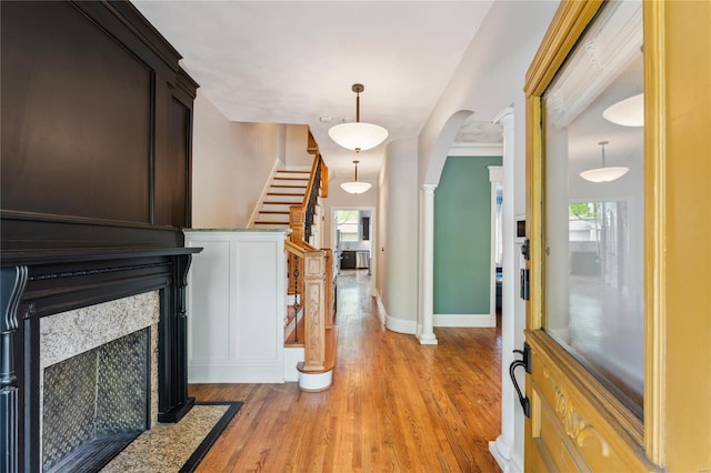 foyer entrance featuring light wood-style flooring, baseboards, arched walkways, decorative columns, and a premium fireplace