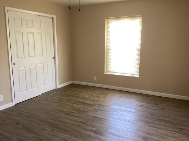 unfurnished bedroom featuring dark wood finished floors, a closet, and baseboards