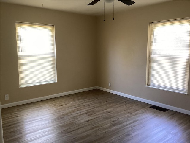 unfurnished room with baseboards, visible vents, dark wood-style floors, and ceiling fan