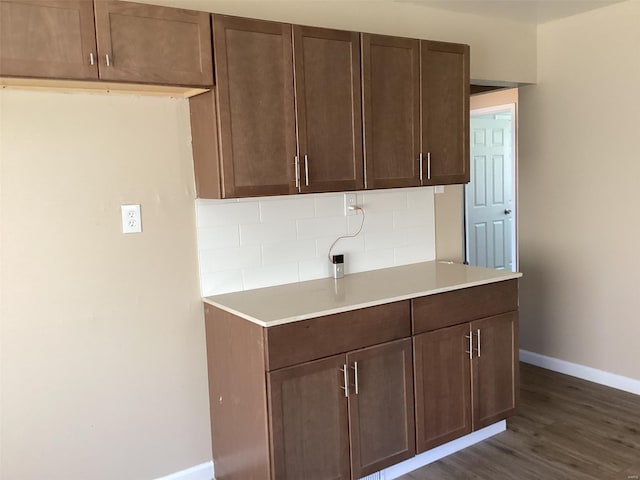 kitchen featuring dark wood-style floors, light countertops, baseboards, dark brown cabinetry, and tasteful backsplash