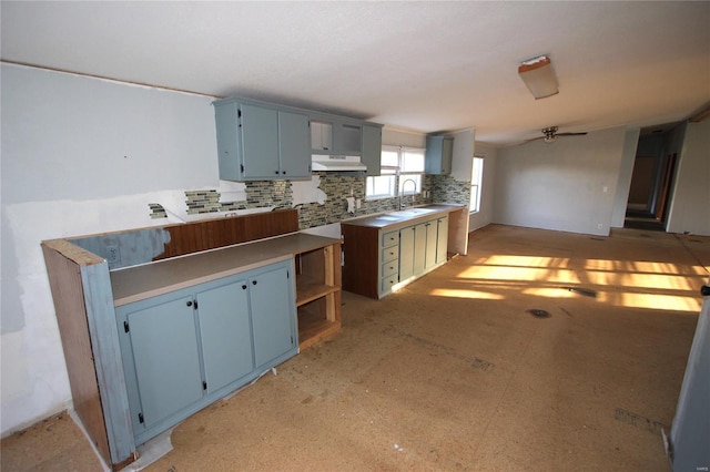 kitchen with under cabinet range hood, a sink, blue cabinets, and decorative backsplash