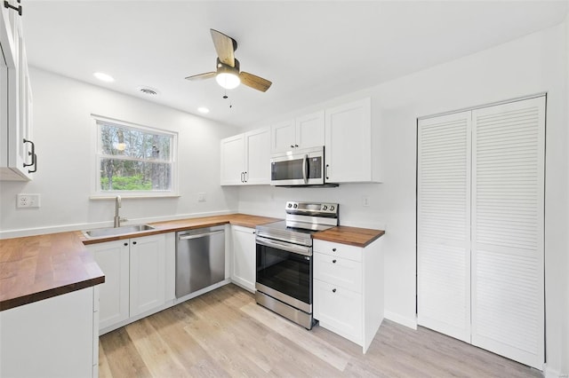 kitchen with stainless steel appliances, a sink, light wood-type flooring, butcher block countertops, and white cabinetry