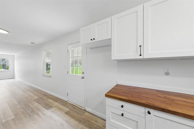 kitchen featuring light wood-style flooring, baseboards, wooden counters, and white cabinetry