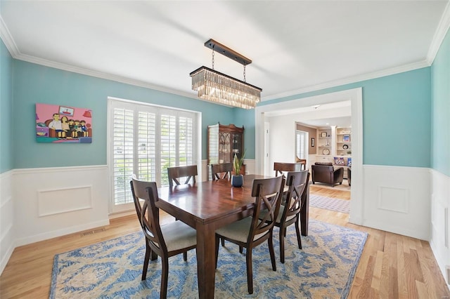 dining area featuring ornamental molding, a wainscoted wall, a chandelier, and light wood-style floors