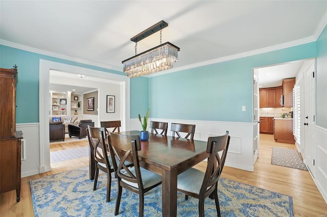 dining space with a notable chandelier, light wood-style floors, a wainscoted wall, ornamental molding, and built in features