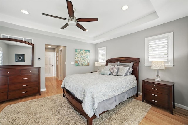 bedroom featuring recessed lighting, light wood-style flooring, baseboards, visible vents, and a raised ceiling