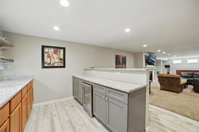 kitchen featuring light wood-style flooring, beverage cooler, open floor plan, a peninsula, and gray cabinets