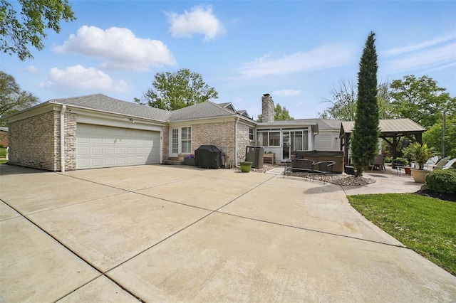 view of front of property with concrete driveway, a gazebo, a chimney, a hot tub, and a garage