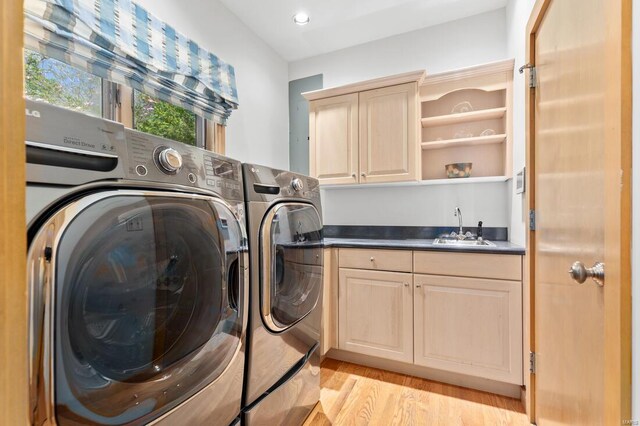 laundry area with light wood finished floors, a sink, washing machine and dryer, cabinet space, and indoor wet bar