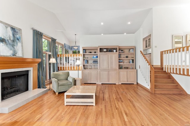 living area featuring light wood finished floors, baseboards, lofted ceiling, stairs, and a fireplace