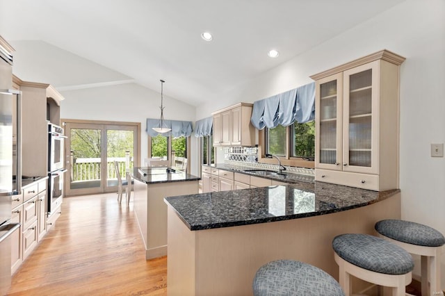kitchen with a sink, light wood-style floors, lofted ceiling, stainless steel double oven, and a kitchen island