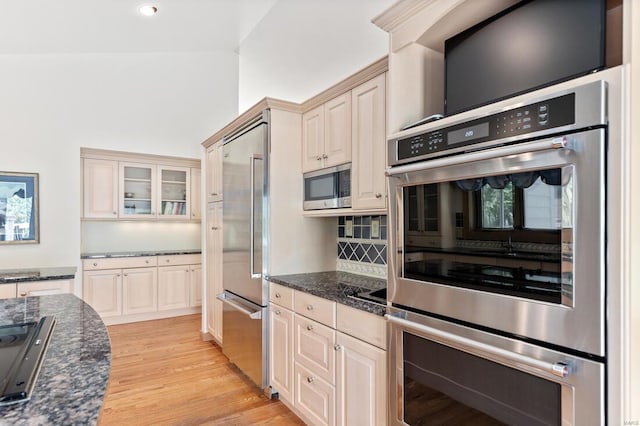 kitchen featuring dark stone countertops, decorative backsplash, built in appliances, light wood-style flooring, and cream cabinetry