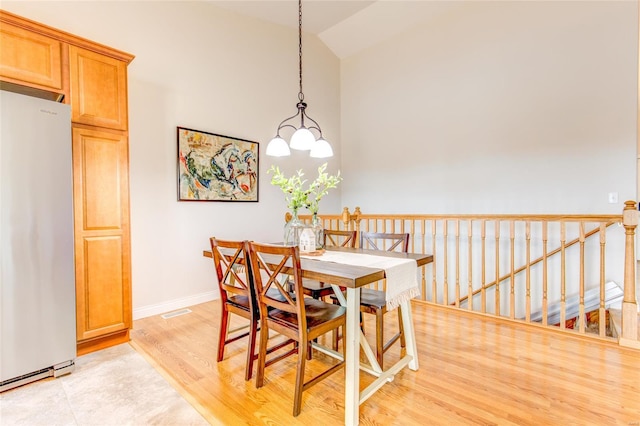 dining room with baseboards, visible vents, light wood finished floors, and high vaulted ceiling