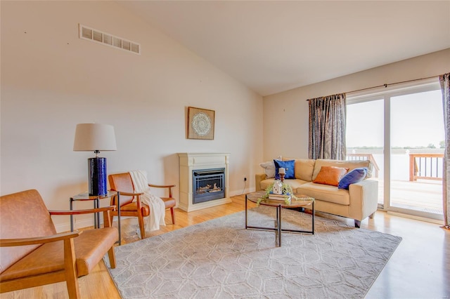 living room with light wood finished floors, a glass covered fireplace, baseboards, visible vents, and lofted ceiling