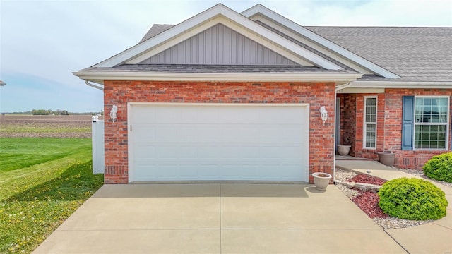 view of front facade featuring roof with shingles, a front lawn, driveway, brick siding, and a garage