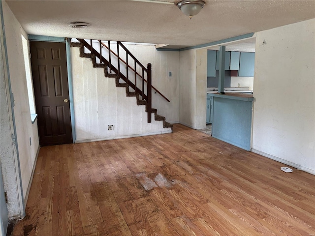 unfurnished living room featuring hardwood / wood-style floors, baseboards, a textured ceiling, and stairs