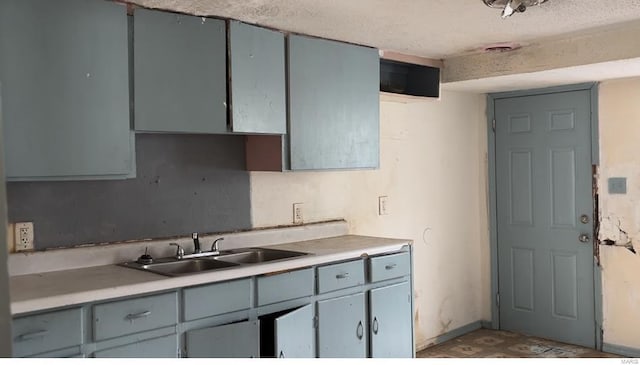 kitchen with light countertops, gray cabinets, a sink, baseboards, and a textured ceiling