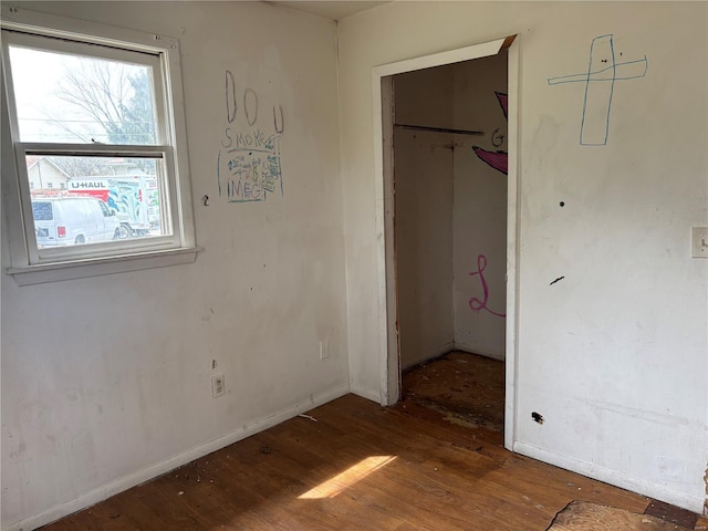 unfurnished bedroom featuring a spacious closet, wood finished floors, a closet, and baseboards