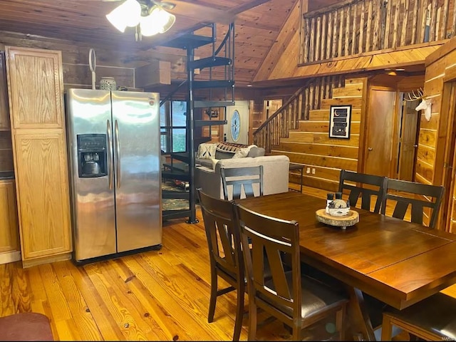 dining room featuring wood ceiling, light wood-style flooring, wooden walls, a ceiling fan, and stairs