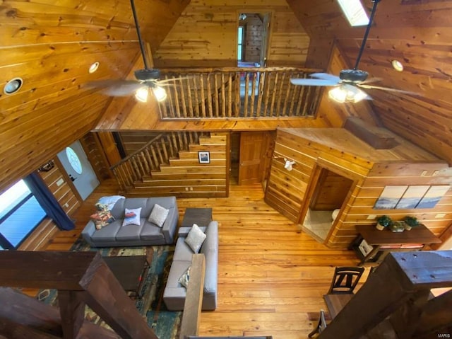 living room featuring wood walls, a ceiling fan, vaulted ceiling with skylight, and wood-type flooring