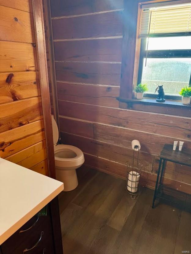 bathroom with wooden walls, wood finished floors, toilet, and vanity