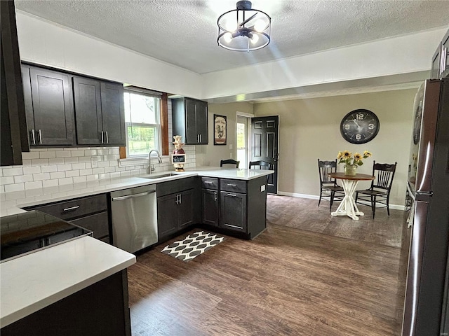 kitchen with tasteful backsplash, a sink, a textured ceiling, a peninsula, and appliances with stainless steel finishes
