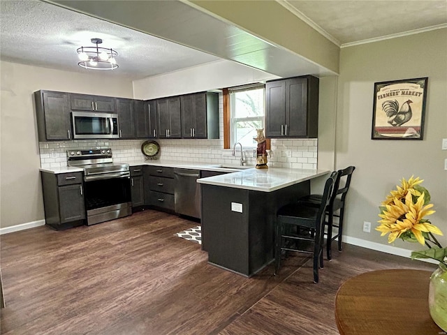 kitchen with a sink, a peninsula, tasteful backsplash, appliances with stainless steel finishes, and a breakfast bar area