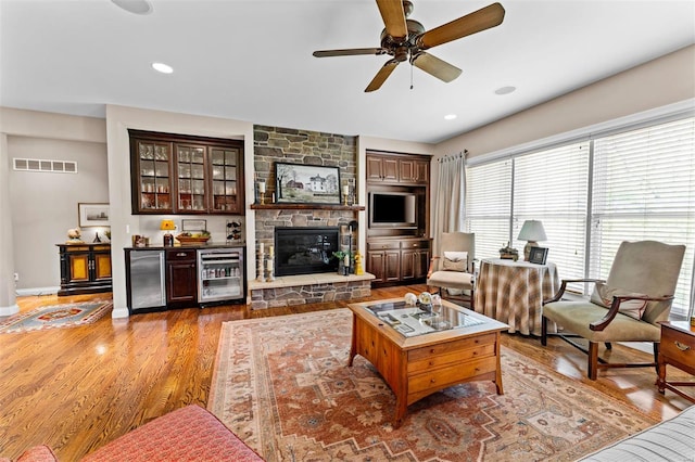 living area with wine cooler, a ceiling fan, visible vents, baseboards, and wood finished floors