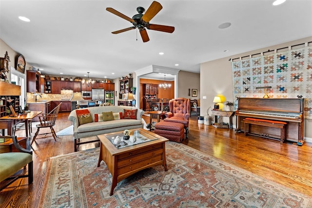 living room featuring baseboards, recessed lighting, wood finished floors, and ceiling fan with notable chandelier