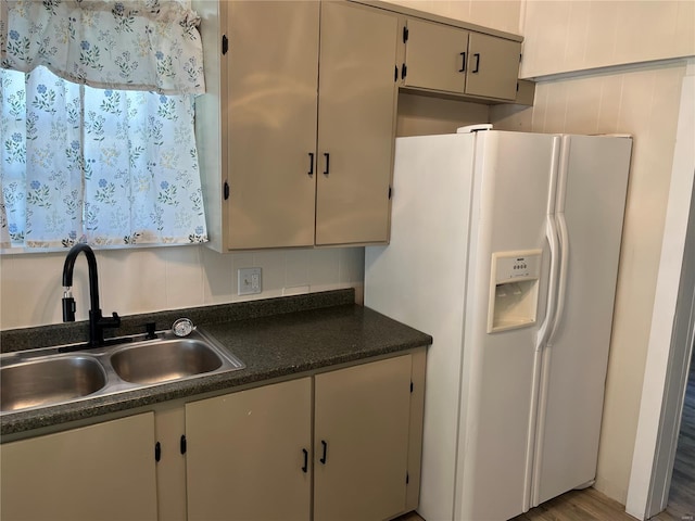 kitchen with backsplash, dark countertops, a sink, and white fridge with ice dispenser