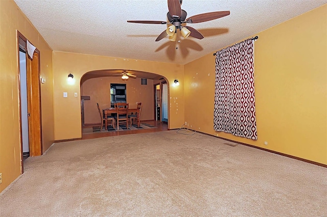 carpeted spare room featuring ceiling fan, arched walkways, and a textured ceiling