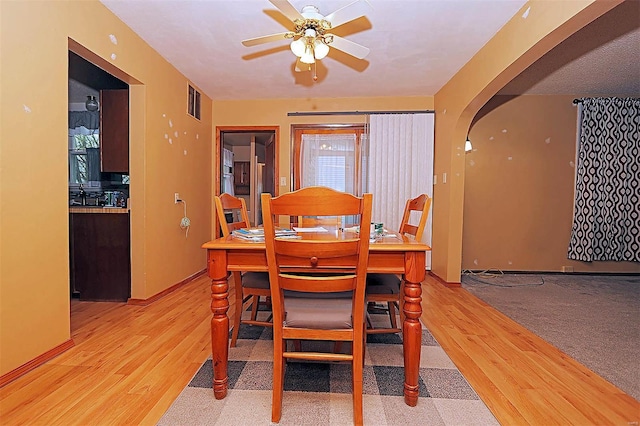 dining area featuring arched walkways, light wood-style floors, visible vents, and ceiling fan
