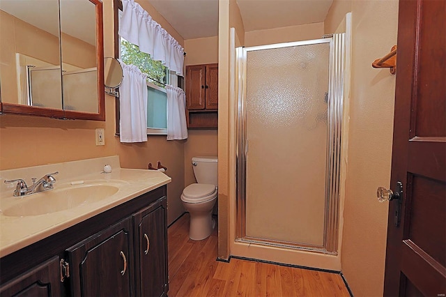 bathroom featuring toilet, wood finished floors, vanity, and a stall shower