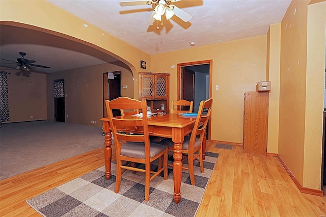 dining room with arched walkways, light wood-style flooring, baseboards, and ceiling fan