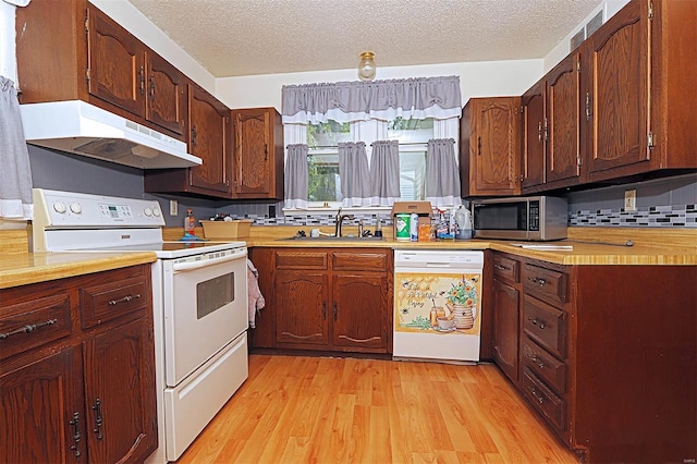 kitchen with a sink, light wood-style floors, white appliances, light countertops, and under cabinet range hood
