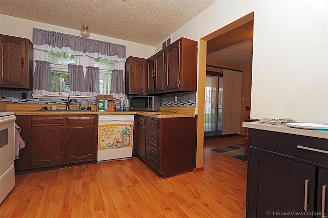 kitchen with light countertops, a sink, stainless steel microwave, light wood-type flooring, and dishwasher