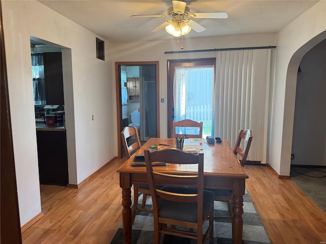 dining space featuring ceiling fan, arched walkways, light wood finished floors, and baseboards