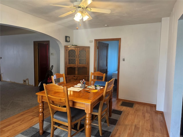 dining room with arched walkways, visible vents, light wood finished floors, and a ceiling fan