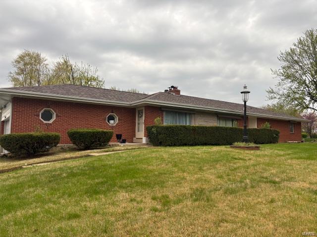 ranch-style house with brick siding, a chimney, a front lawn, and a garage