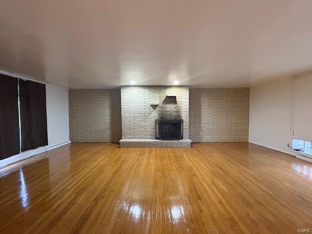 unfurnished living room featuring brick wall, a brick fireplace, and light wood-style flooring