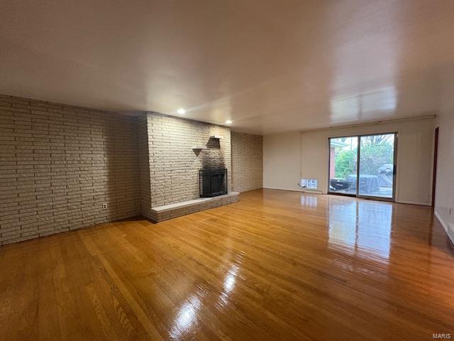 unfurnished living room with wood finished floors, a brick fireplace, and brick wall