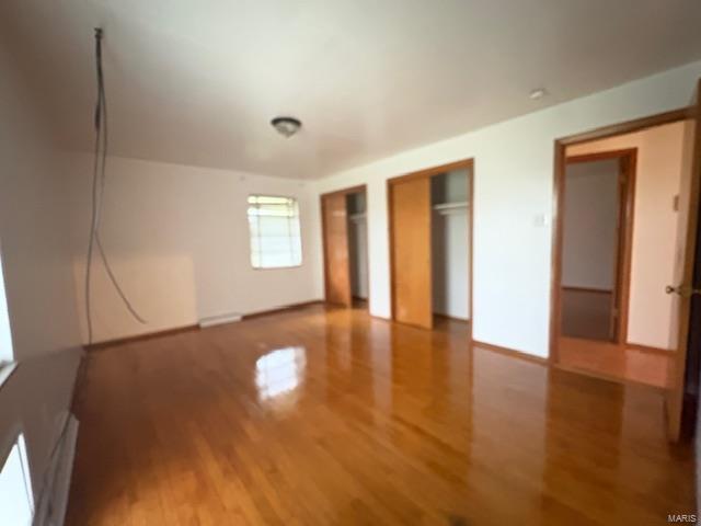 unfurnished bedroom featuring two closets, baseboards, and wood finished floors